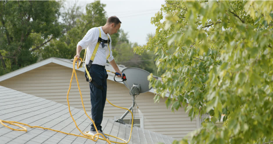 Applicator in a safety harness applying rejuvenation treatment to an asphalt shingle roof